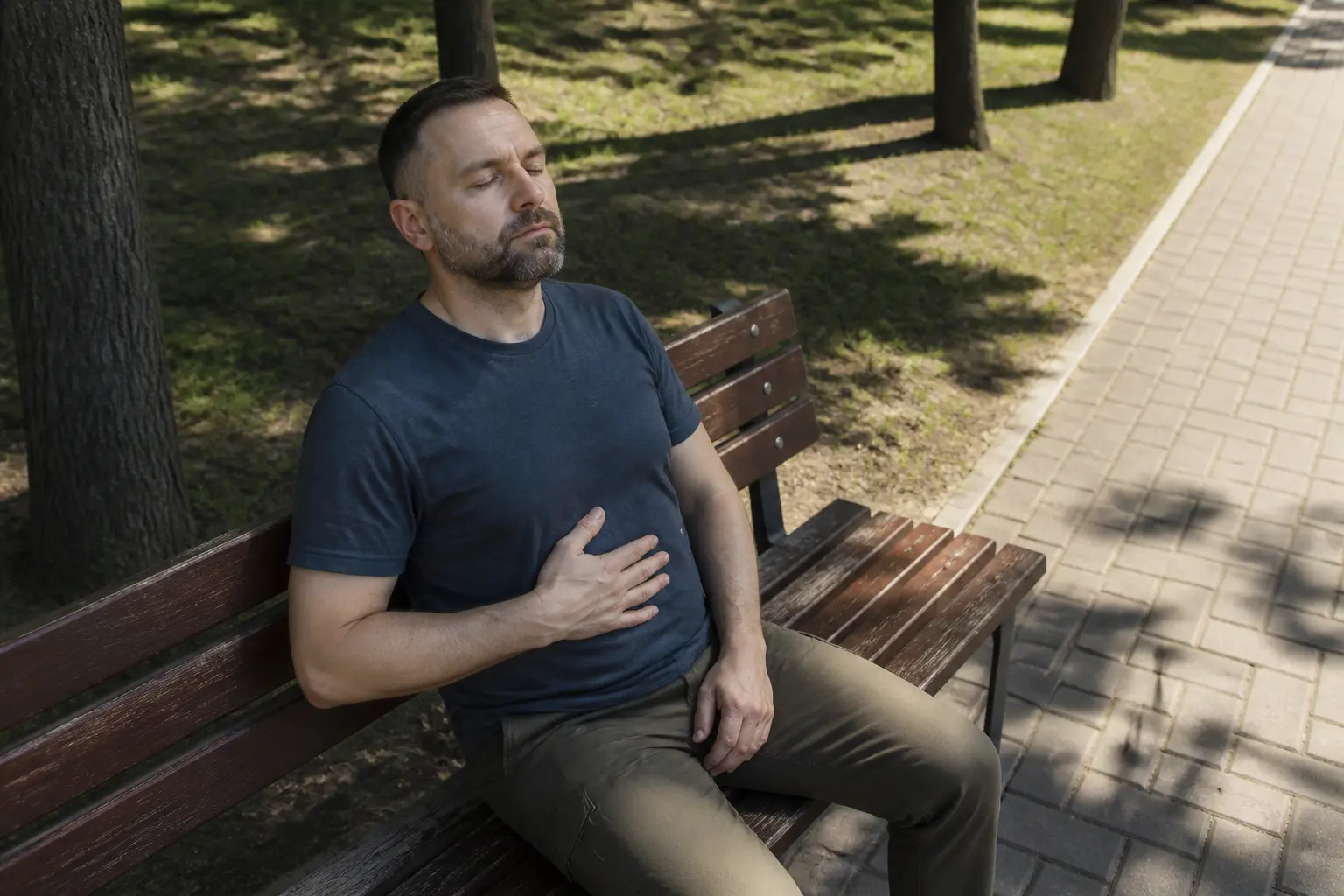 Чоловік на лавці в парку виконує дихальні вправи під час нападу тахікардії